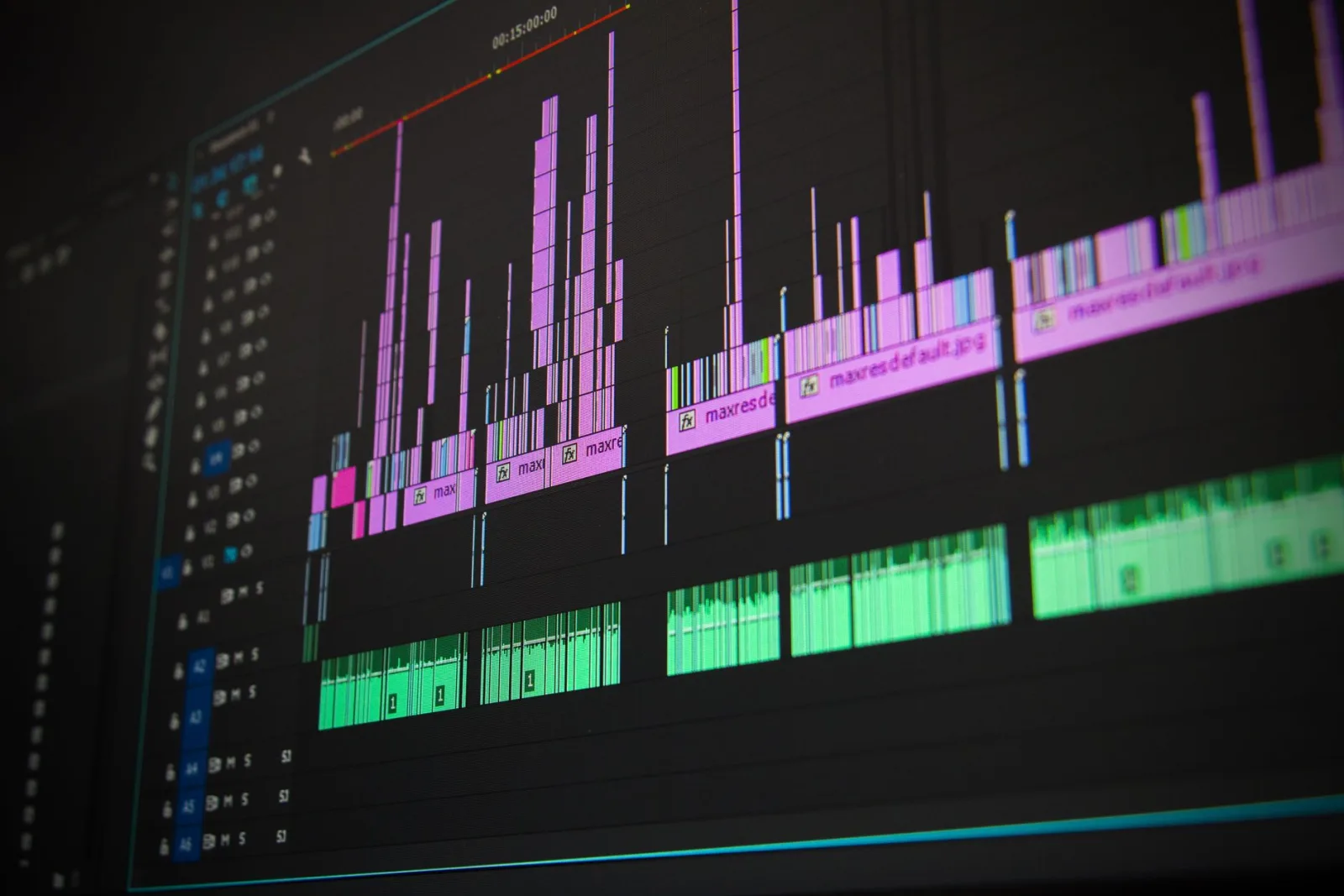 Angled close-up of a video editing timeline on a monitor, with purple video clips above green audio waveforms