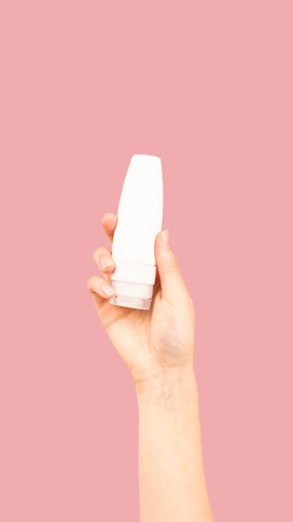 A hand presenting a cosmetic bottle against a pink background